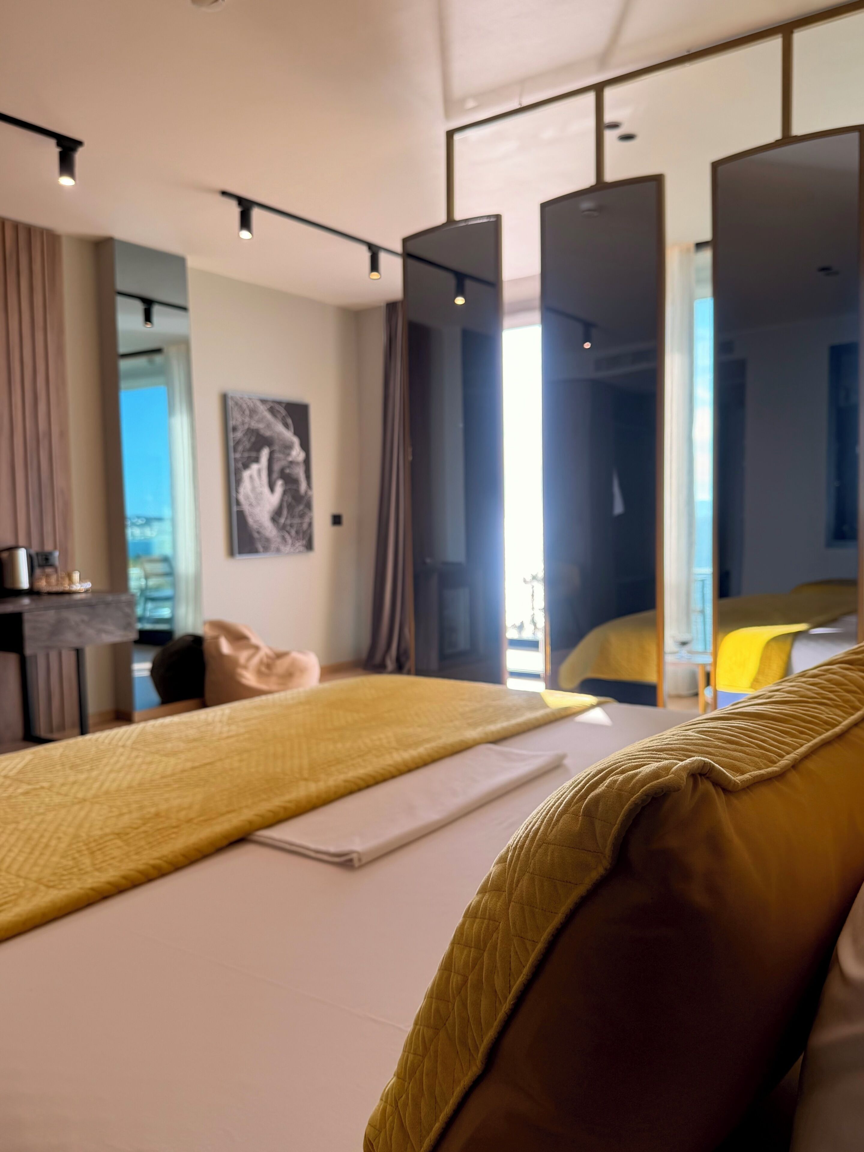 A modern hotel room with a large bed, a desk, a chair, and a view of the outdoors.