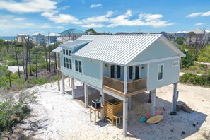 A beachfront house with a balcony, a small deck, and a sandy beach area.