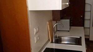 Una cocina compacta con armarios blancos, un lavamanos de acero inoxidable y un horno empotrado.