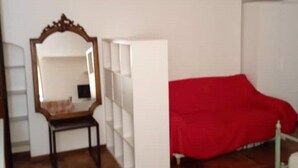 Una habitación con suelo de parqué, un armario blanco, una cama roja y un espejo con marco decorado.
