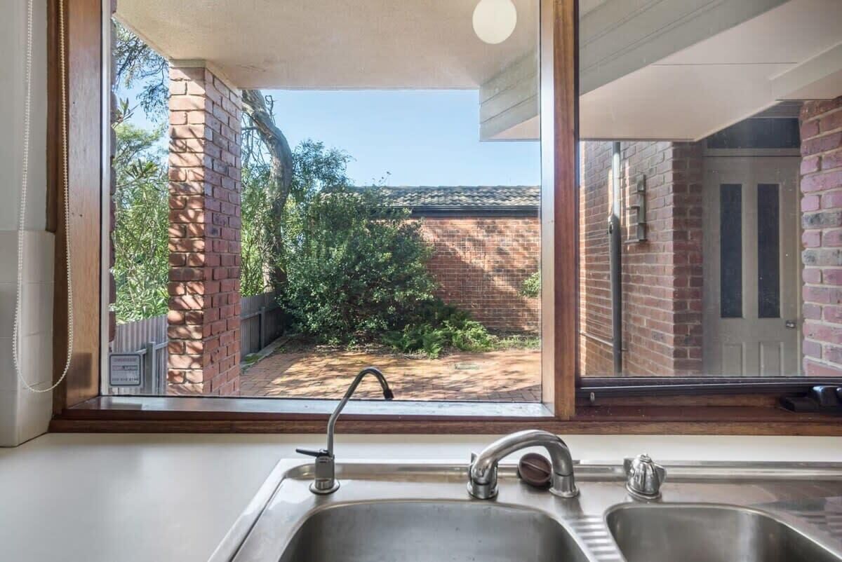 A kitchen with a large window, a sink, and a view of a brick wall and greenery outside.