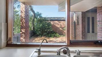 A kitchen with a large window, a sink, and a view of a brick wall and greenery outside.