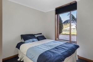 A bedroom with a bed, a window with a view of a building and palm trees, and a door.