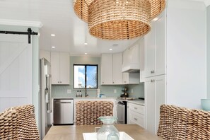 Une cuisine moderne avec des meubles blancs, un réfrigérateur en acier inoxydable et un panier tressé servant de centre de table.