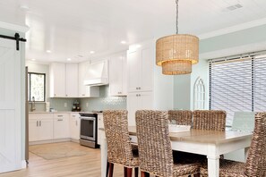 Une cuisine moderne avec des meubles blancs, un four en acier inoxydable et un coin repas agrémenté d’un ensemble de chaises en osier.