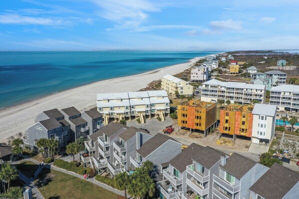 Un quartier résidentiel situé sur la côte, avec des propriétés donnant sur la plage, notamment des immeubles à plusieurs étages et une plage de sable.