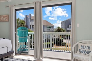 A balcony with a view of neighboring houses, a turquoise Adirondack chair, and a sign reading 'BEACH THERAPY'.
