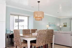 A dining area with a table and chairs, a hanging light fixture, and a sofa in the background.