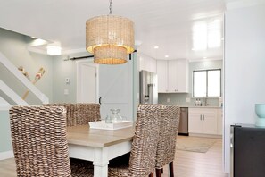Een moderne keuken met witte kasten, een roestvrijstalen koelkast en een eethoek met rieten stoelen en een houten tafel.