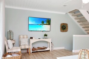 A living room with a flat-screen TV mounted on the wall, a fireplace, a comfortable seating area with a chair and ottoman, and a staircase leading to an upper level.