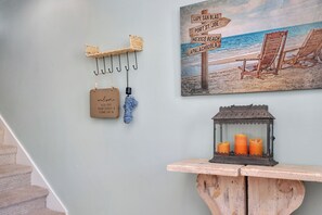 Een muur met een schilderij van een strand, een houten bord met een welkomstboodschap en een kandelaar.