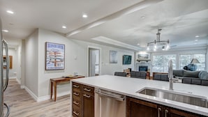 A modern kitchen with a large island, stainless steel appliances, and a dining area with a gray sofa. - Modern and Updated St James Premium 3 Bedroom Residence 3 Condo by RedAwning (Avon)