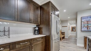 A modern kitchen with dark wood cabinets, a stainless steel refrigerator, and a white countertop. - Modern and Updated St James Premium 3 Bedroom Residence 3 Condo by RedAwning (Avon)
