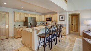 A spacious kitchen with wooden cabinets, a central island with bar stools, a refrigerator, microwave, and a toaster. - Luxury 4 bedroom Premier Residence at St James Place 4 Condo by RedAwning (Avon)