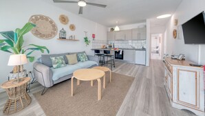 A modern living room with a sofa, two round tables, a ceiling fan, and a kitchen in the background. - Chez Carmen • Pool View • Beach 900M • LVH (Puerto del Carmen)