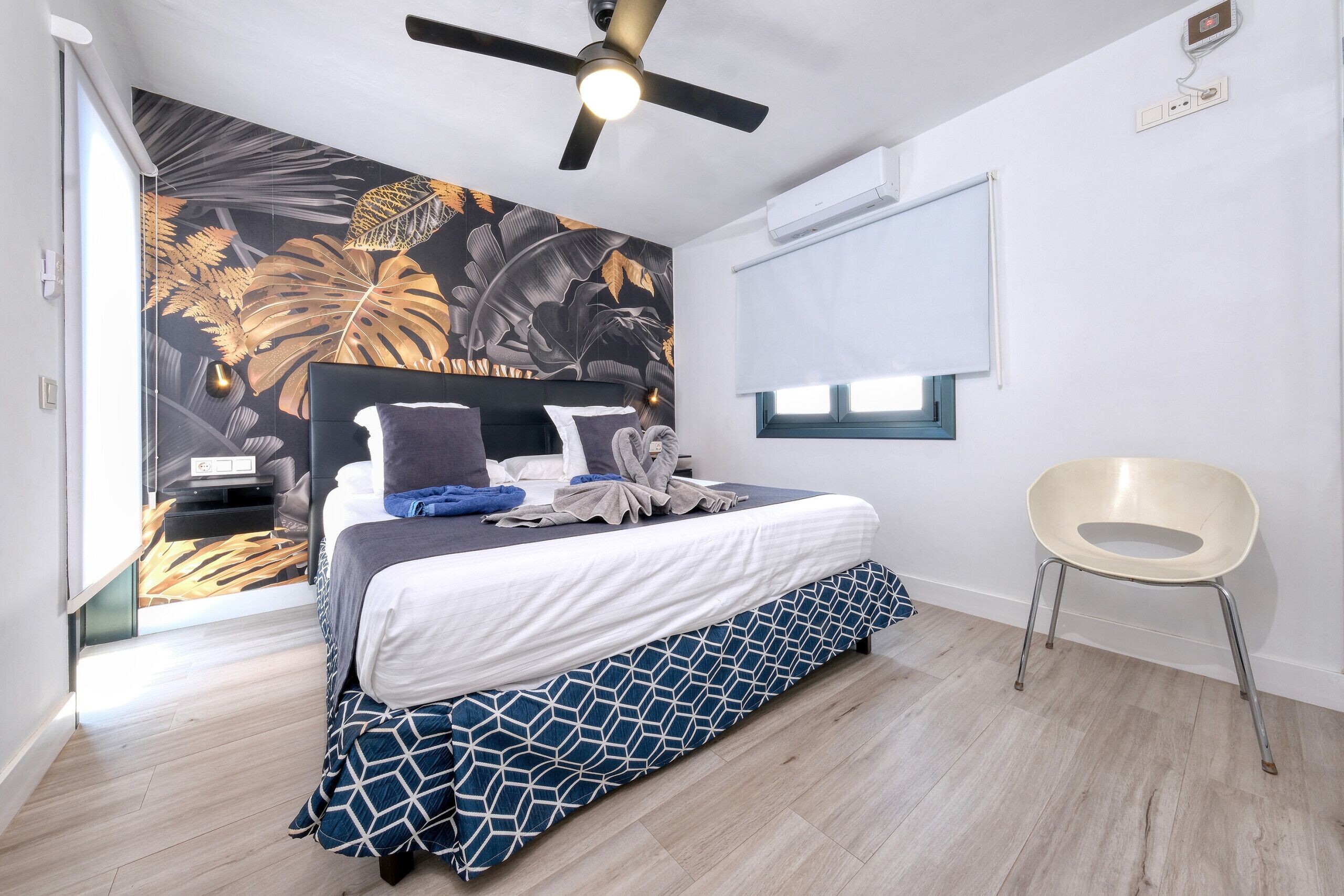 Une chambre moderne avec un lit, un ventilateur de plafond, une fenêtre et une chaise.