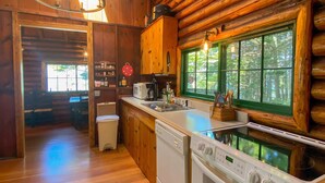 A log cabin interior with a kitchen area, wooden floors, and a dining area. - Charming 4-Bedroom Linekin Log Cabin in Boothbay, ME with stunning waterfront views. (Boothbay)