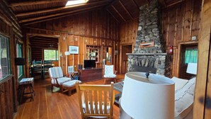 A log cabin interior with a stone fireplace, wooden furniture, and a television. - Charming 4-Bedroom Linekin Log Cabin in Boothbay, ME with stunning waterfront views. (Boothbay)