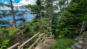 A wooden staircase leading to a forested area with a view of a lake. - Charming 4-Bedroom Linekin Log Cabin in Boothbay, ME with stunning waterfront views. (Boothbay)