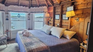 A cozy cabin bedroom with a large bed, a view of the water through windows, and wooden walls. - Experience lakeside luxury at Piffi Biff, a spacious 5-bedroom cabin on Southport, ME. (Southport)