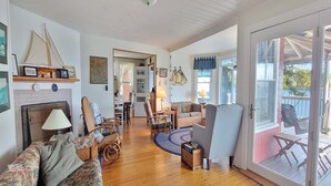 A spacious living room with a fireplace, wooden flooring, and a view of the outdoors through a glass door. - Experience lakeside luxury at Piffi Biff, a spacious 5-bedroom cabin on Southport, ME. (Southport)