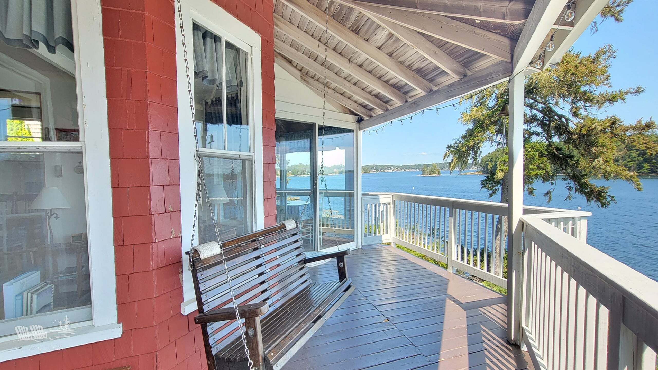 Una terraza de madera con un banco, una puerta de vidrio que da a una habitación y vistas a un lago.