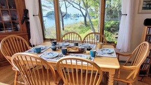 A dining table with chairs, plates, cups, and a view of a lake. - Experience coastal charm at Merwick Cottage in Georgetown, ME, with 3 bedrooms and waterfront views. (Georgetown)