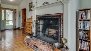 A room with a fireplace, wooden bookshelves, and a door leading to a porch. - Experience coastal charm at Merwick Cottage in Georgetown, ME, with 3 bedrooms and waterfront views. (Georgetown)