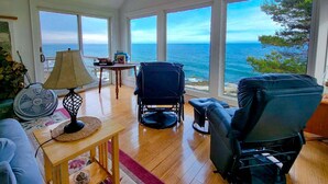 A living room with a view of the ocean, a fan, a lamp, and a chair. - Your Tranquil Indian Point Retreat with Breathtaking Views & Beach Access (Georgetown)