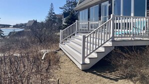 A coastal house with a deck, large windows, and a view of the sea.