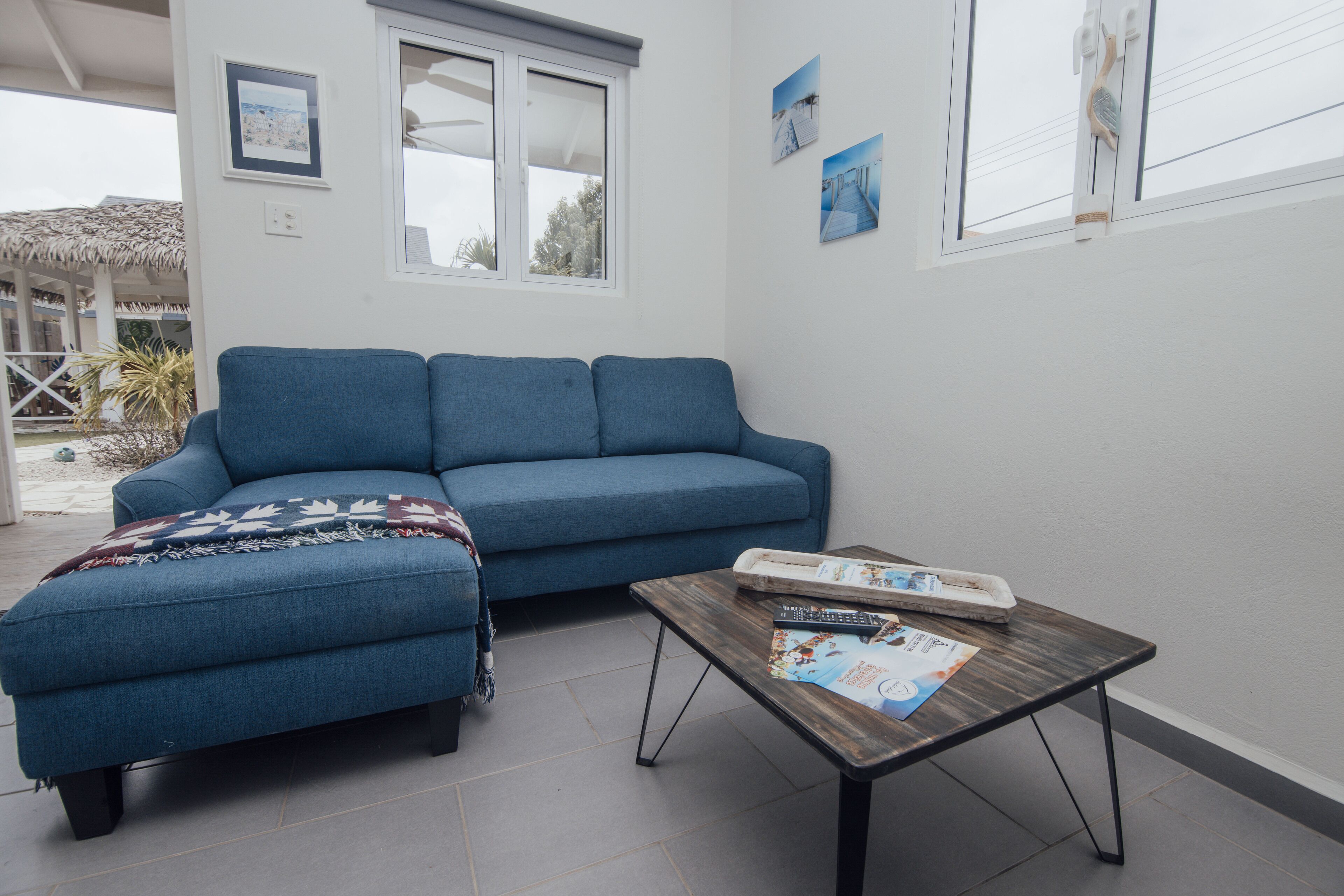 Een woonkamer met een blauwe bank, een houten salontafel en een raam met zonwering.