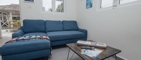 Een woonkamer met een blauwe bank, een houten salontafel en een raam met zonwering.