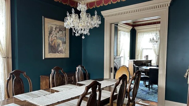 Une salle à manger avec une grande table, des chaises, un lustre et un tableau au mur.