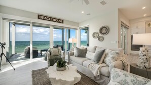 A spacious living room with a large window overlooking the ocean, a comfortable sofa set, and a coffee table.