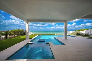 A swimming pool with a view of the ocean, surrounded by a white fence and a covered patio area.