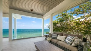A covered outdoor seating area with a view of the ocean, a wicker sofa with cushions, and a wooden table.