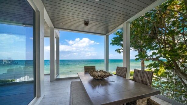 A spacious dining area with a view of the ocean, featuring a wooden table and wicker chairs.