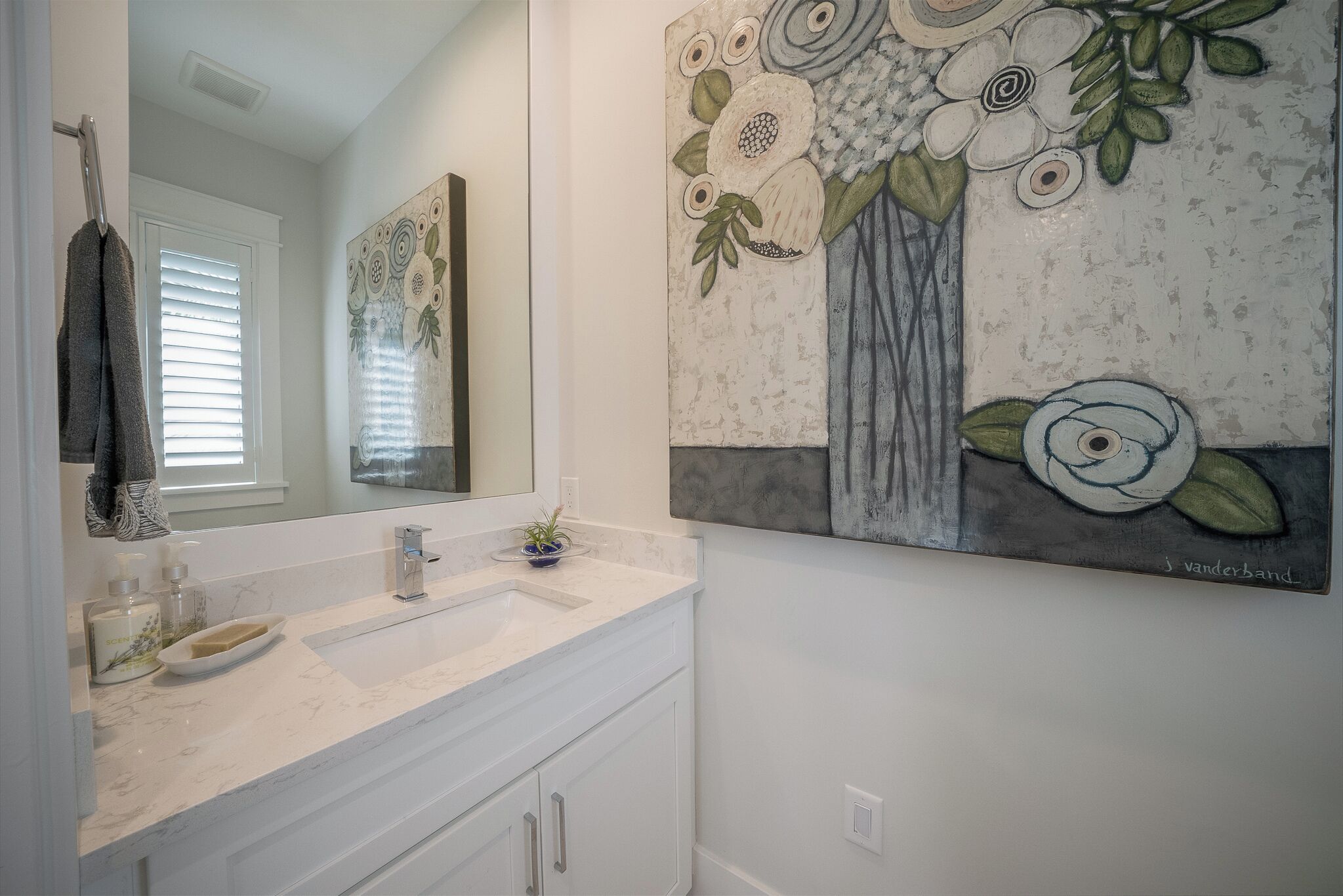 A bathroom with a white vanity, a mirror, and a floral artwork on the wall.