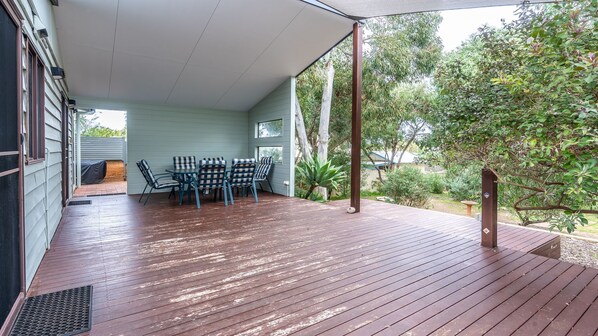 Een overdekt terras met een houten terras, een tafel met stoelen en uitzicht op de omliggende begroeiing.