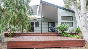 A modern house with a wooden deck, a covered outdoor seating area, and a garden with various plants.