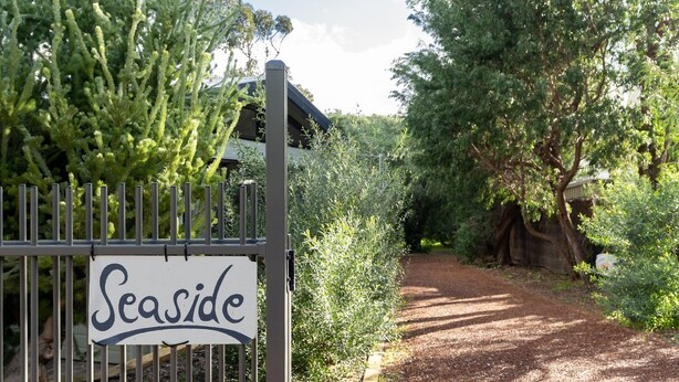 A sign reading "Seaside" at the entrance of a path surrounded by greenery.