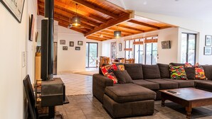 A spacious living room with a large sectional sofa, a wooden coffee table, and a fireplace. There are framed pictures on the walls and a dining area in the background.