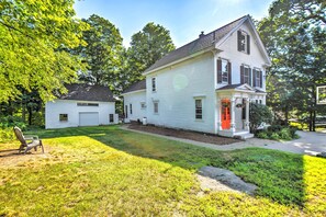A two-story white house with a red door, a front porch, and a small attached garage. - Hot Tub + Walk to Lakeside Dining: Meredith Home! (Meredith)