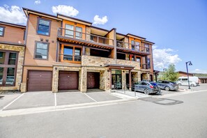 A multi-story building with a stone facade, multiple balconies, and a parking area with several cars. - Blue River Flats Retreat: Stunning Getaway With Amazing Views (Silverthorne)