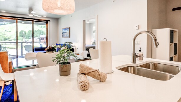 A modern kitchen with a large island, stainless steel sink, and a hanging pendant light. - Blue River Flats Retreat: Stunning Getaway With Amazing Views (Silverthorne)