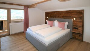A bedroom with a large bed, wooden ceiling beams, a wooden headboard, and a view through a window. - Panoramablick by Interhome (Mayrhofen)