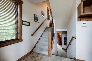 A staircase with wooden handrails, carpeted steps, and a wall-mounted thermostat.