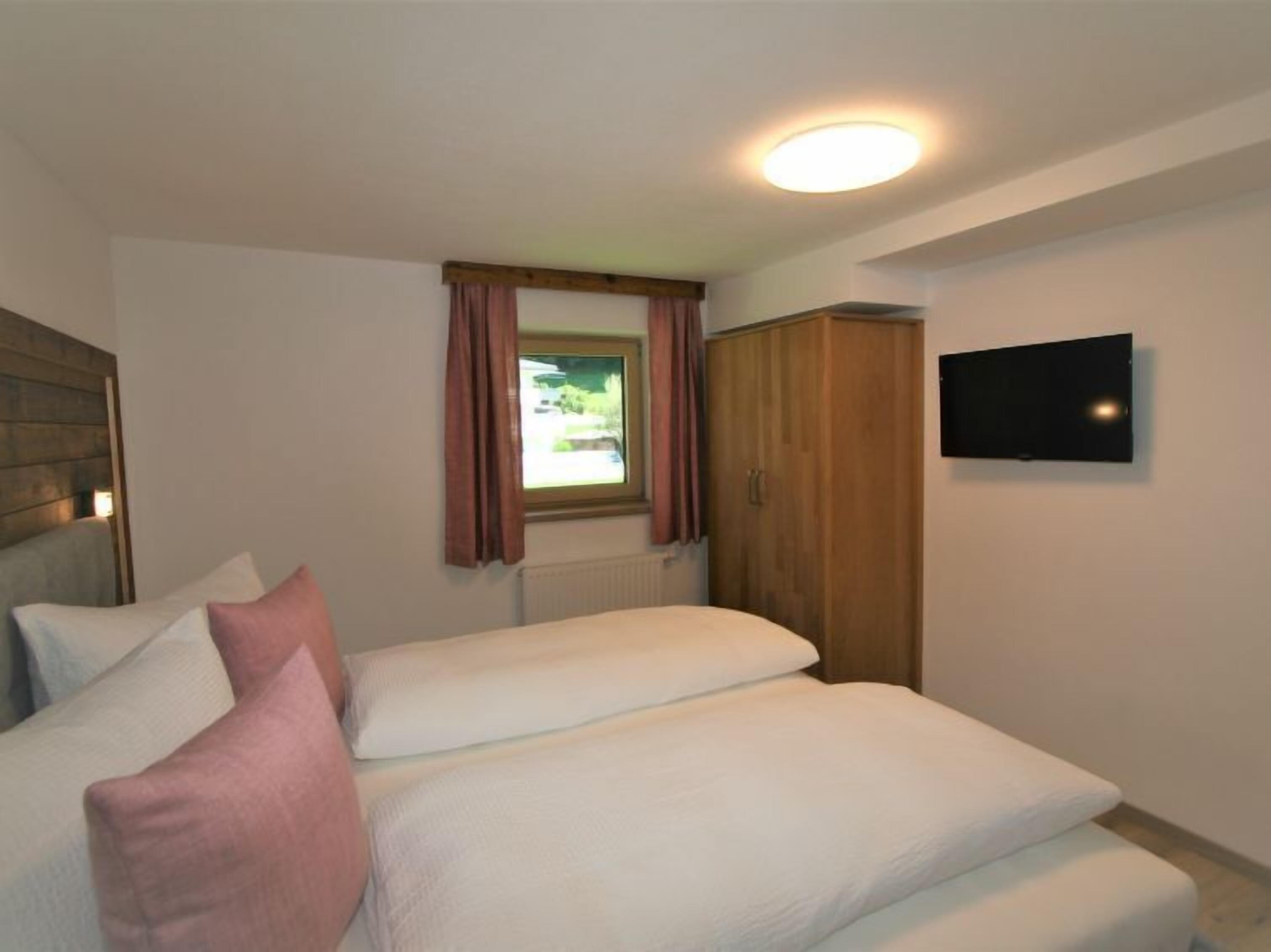 Un dormitorio con dos camas, un armario, televisor y ventana con cortinas.