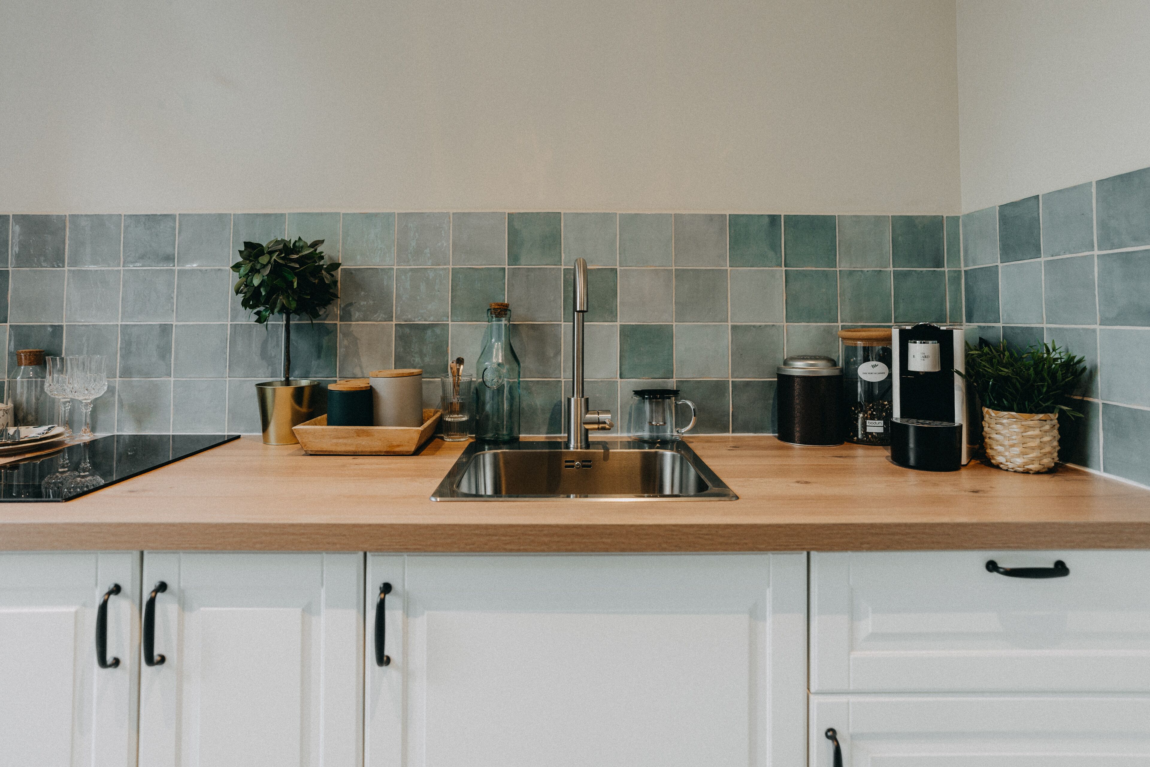 A kitchen with a stainless steel sink, white cabinets, and a wooden countertop.