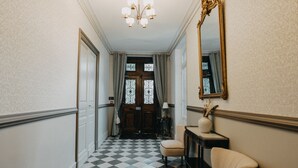 Un couloir doté d’un sol à carreaux, d’un lustre, d’un miroir et d’une porte ornée de vitraux.